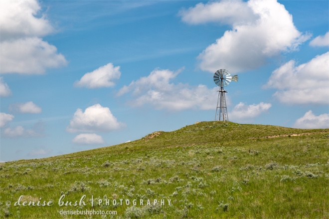An old-fashioned windmill spins in the breeze atop a grassy hill.