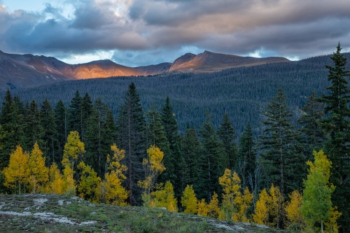 A border of golden aspen trees compliments the warm spotlight on the distant mountains.