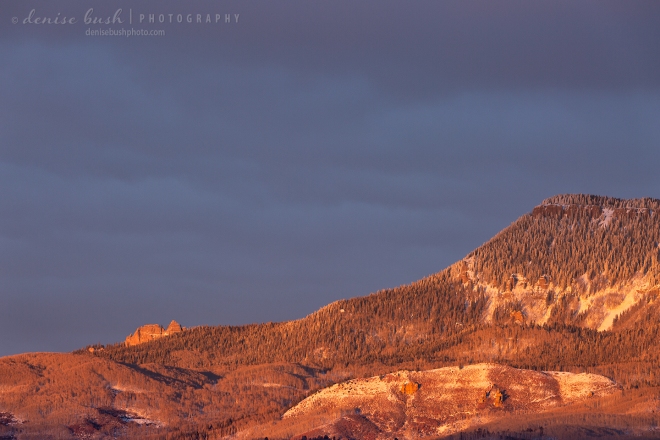 A narrow gap in the clouds allows the end of Cimarron Ridge and Castle Rock light up at sunset.
